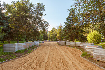 Preparation of the road foundation in the park. Sand leveling. Packages with paving slabs are prepared on the lawn.