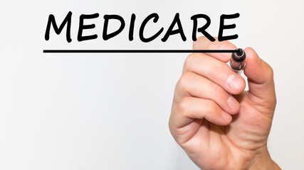 the hand writes the Word MEDICARE with a marker on a white background. business concept