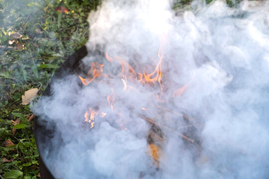 Burning in  barrel of autumn yellow maple leaves with flames and charcoals, the view from above, a lot of smoke, goodbay autumn summer, autumn mood