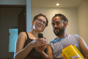 Pareja de novios casados comiendo palomitas viendo television pelicula en casa comodos