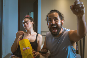 Pareja de novios casados comiendo palomitas viendo television pelicula en casa comodos
