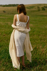 Nice picnic on the grass. Young beautiful woman in the middle of green field. Summer landscape, good weather. Windy day with sun and clouds. Cotton white suit eco style. 