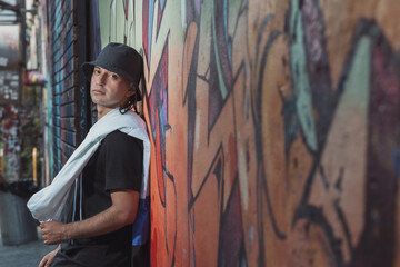Mexican Latin young man leaning on the wall, urban portrait wearing black hat