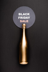 Top view of golden bottle of champagne near circle with black friday sale lettering on black background