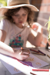 Fototapeta premium young girl child seated at her outdoor study desk at home learning school from home with colored pencils paper drawing learning in the sunshine