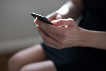 View of a woman seated wearing a black dress holding her mobile phone cell using it to keep up to date 