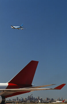 Close-up Of Airplane's Tail Fin Flying Plane In Background