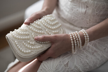 A woman wearing a string of pearls as a bracelet a pearl covered purse dressed in a white lace...