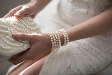 A woman wearing a string of pearls as a bracelet a pearl covered purse dressed in a white lace...