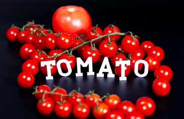 A large red tomato and clusters of cherry tomatoes on a dark background. Between the fruits is the inscription TOMATO.