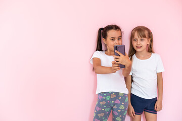 Two little girls playing with smartphones on a pink background