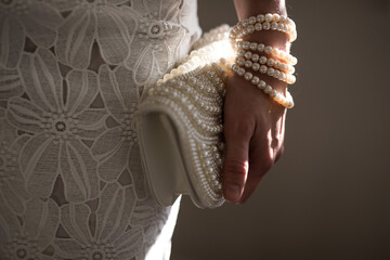 A woman wearing a string of pearls as a bracelet a pearl covered purse dressed in a white lace...