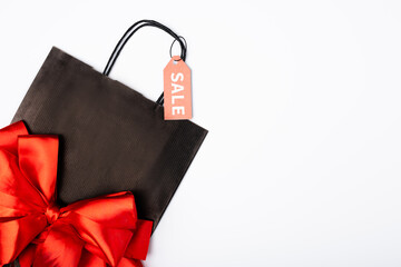 Top view of black shopping bag with bow and price tag with sale lettering on white background