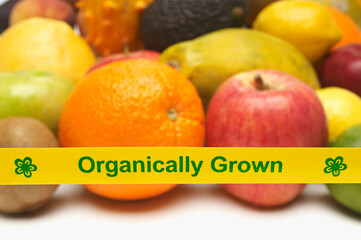 Closeup of organically grown fruits behind yellow tape over white background