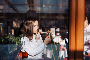 The girl sits in the cafe and paints her lips with lipstick.