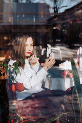 The girl sits in the cafe and paints her lips with lipstick.