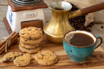 A cup of coffee, cookies, cinnamon, coffee beans, a mill and a coffee maker on a wooden table. Still life.
