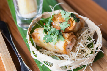 Close up of fried spring rolls in a woven basket with decorative food. Selective focus.