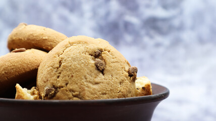 Soft freshly baked cookies with chocolate chips in a brown earthenware plate on gray marble. American traditional sweet pastry pastry, delicious homemade dessert. Culinary background.