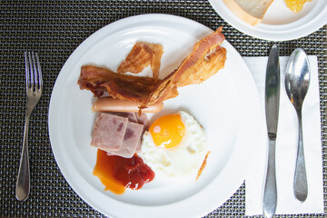 American breakfast with fried eggs, bacon, ham, sausage on white plate.