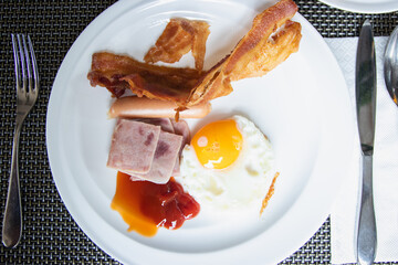 American breakfast with fried eggs, bacon, ham, sausage on white plate.