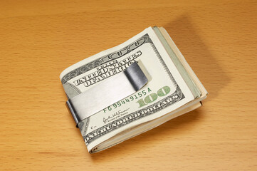 US currency in silver money clip on wooden table