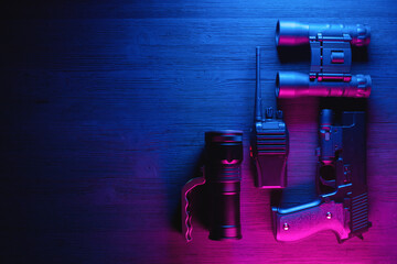 Spy secret service agent desk table concept background. Gun, radio, binoculars and flashlight on the neon background with copy space.