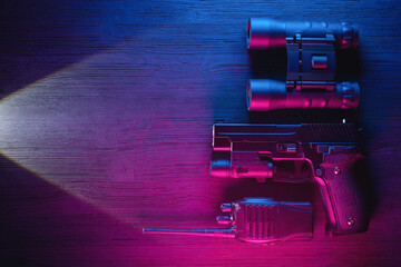 Spy secret service agent desk table concept background. Gun, radio, binoculars and flashlight on the neon background with copy space.
