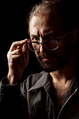 Dark studio portrait of a middle-aged man with beard in glasses