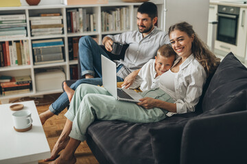 young family sitting on sofa and using laptop computer at home