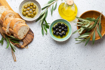 Green and black olives with olive oil in a glass bottle, olive tree sprigs and cut fresh ciabatta...