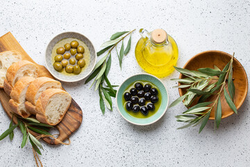 Green and black olives with olive oil in a glass bottle, olive tree sprigs and cut fresh ciabatta...