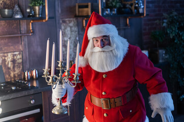 Santa claus sneaks up at night and holding a candelabrum. - obrazy, fototapety, plakaty