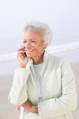 Senior woman stands on beach talking on mobile phone