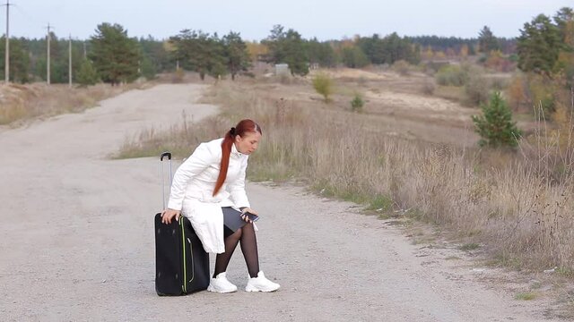 a lonely woman with a suitcase is walking on an empty road without a cellular connection, trying to catch a phone signal