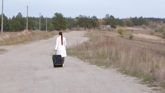a lonely woman with a suitcase is walking on an empty road, the concept of travel, to be in an unknown place alone