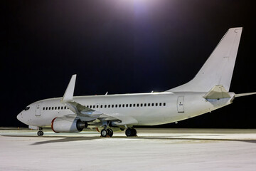 White passenger aircraft on the night airport apron at winter