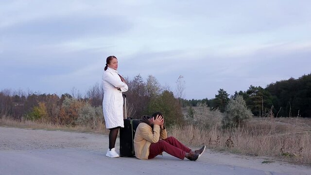 a man and a woman get lost, travelers with a suitcase on an empty road, a woman comforts her upset husband