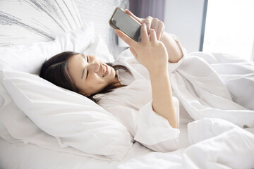Asian Woman Using Social Media on Mobilephone While Lying Down in Bed