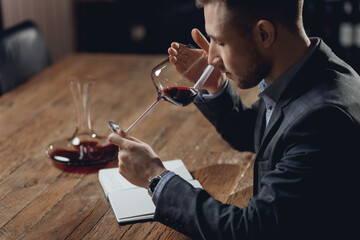 Sommelier compiles tasting card of alcohol for restaurant, evaluates red wine in glass