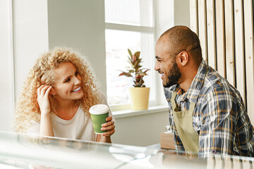 Smiling blonde woman talking to a waiter of a coffee shop at the counter