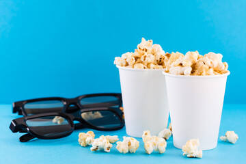 Home cinema. Caramel popcorn in paper cups and 3D glasses on a blue background