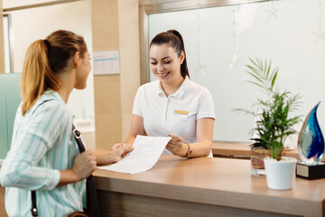 Happy receptionist talking to a customer at health spa. - obrazy, fototapety, plakaty