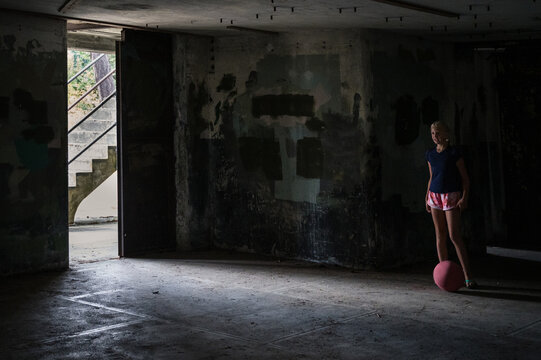 Sporty young girl preparing to kick a kickball in a dark room