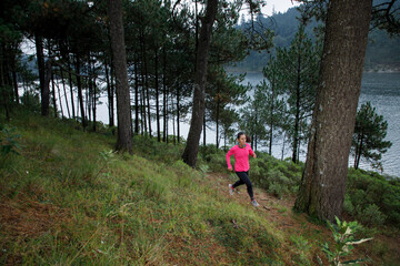 Mujer corriendo en el bosque, subiendo montañas con un lago al fondo