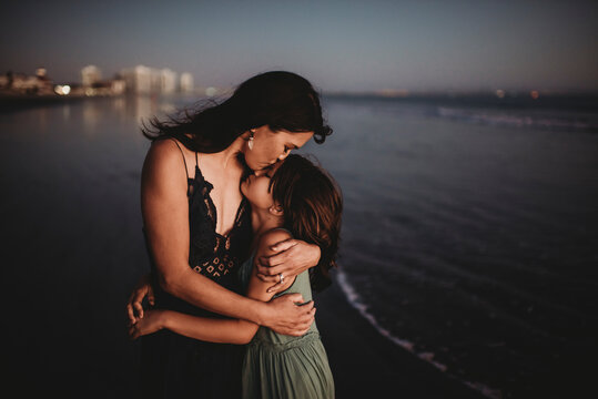 Tender mother hugging and kissing 8 yr old daughter on beach at sunset