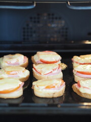 Hot homemade sandwiches with sausage, tomatoes and cheese on a baking sheet in the kitchen oven.Natural healthy food.