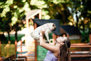 Happy dog ​​and girl. The girl is playing with a dog. Young woman walking with a pug dog in summer park. Portrait of a pug. Portrait of a beautiful pug puppy. The dog is lying on the ground.