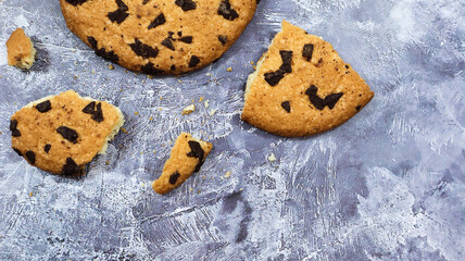 One soft freshly baked chocolate chip cookie with crumbs and chunks on a gray marble kitchen countertop. American traditional pastry, dessert. Delicious sweet food. Flat lay.