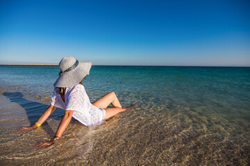 Woman with white hat relax on the beach. Happy lifestyle. Blue sky,white sand and crystal sea of tropical beach. Vacation on Paradise island at Red sea near city Hurghada in Egypt